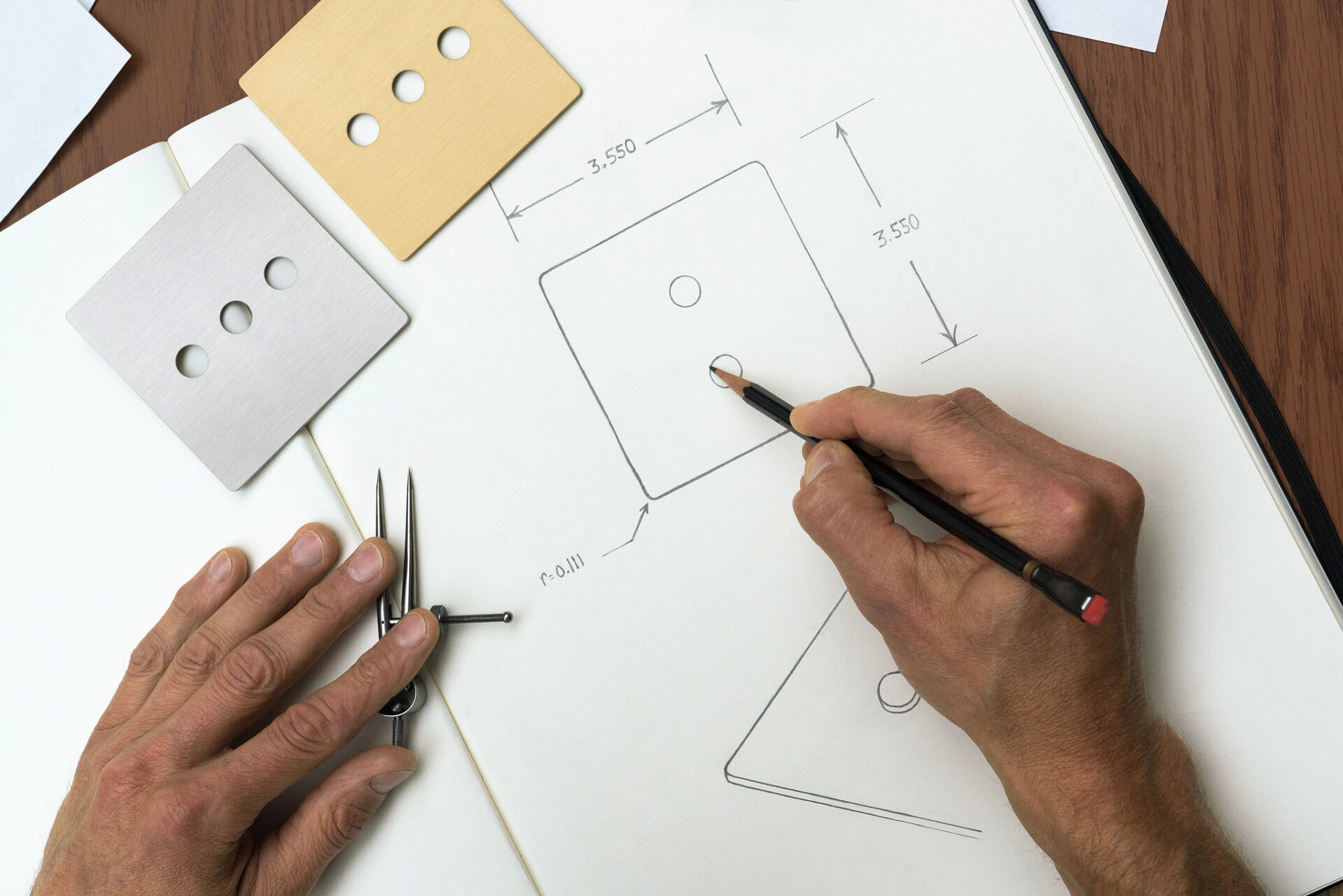 A person sketches a design on paper using a pencil, surrounded by geometric templates and a compass, measuring dimensions precisely for a project.