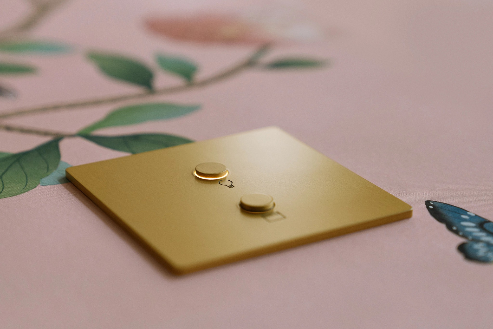 A gold-colored square with protruding shapes on decorative wallpaper featuring flowers and a butterfly. Elegant and minimalistic design.