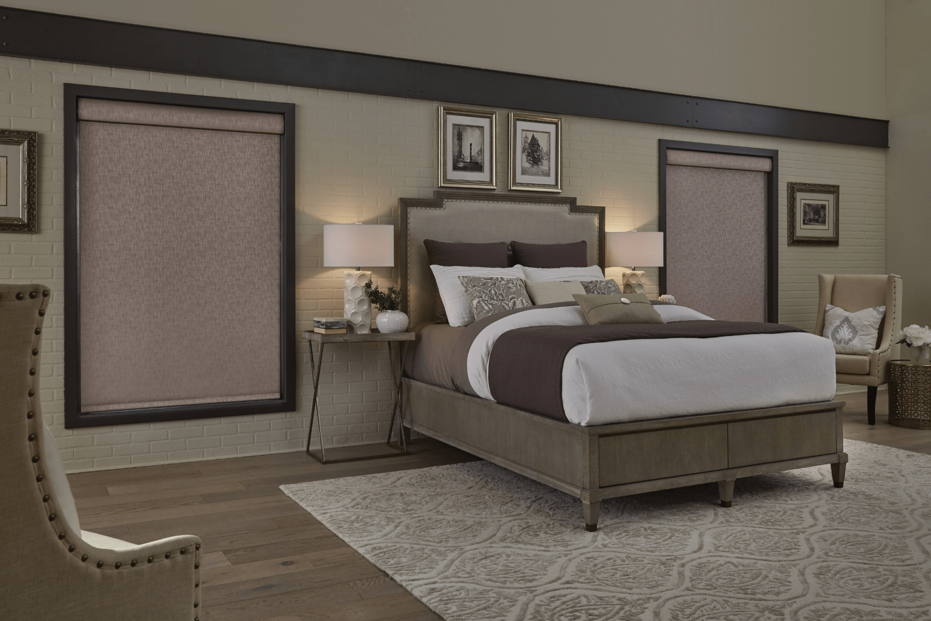 A cozy bedroom features a large bed with neutral tones, elegant chairs, framed artwork, soft lighting, and patterned rug creating a sophisticated ambiance.