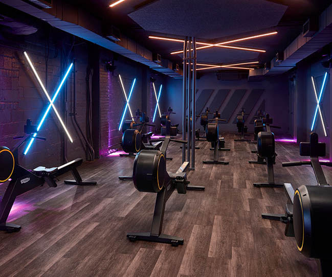 A modern indoor gym with rowing machines, neon lights, and wooden flooring, creating a dynamic and energetic atmosphere for workouts.