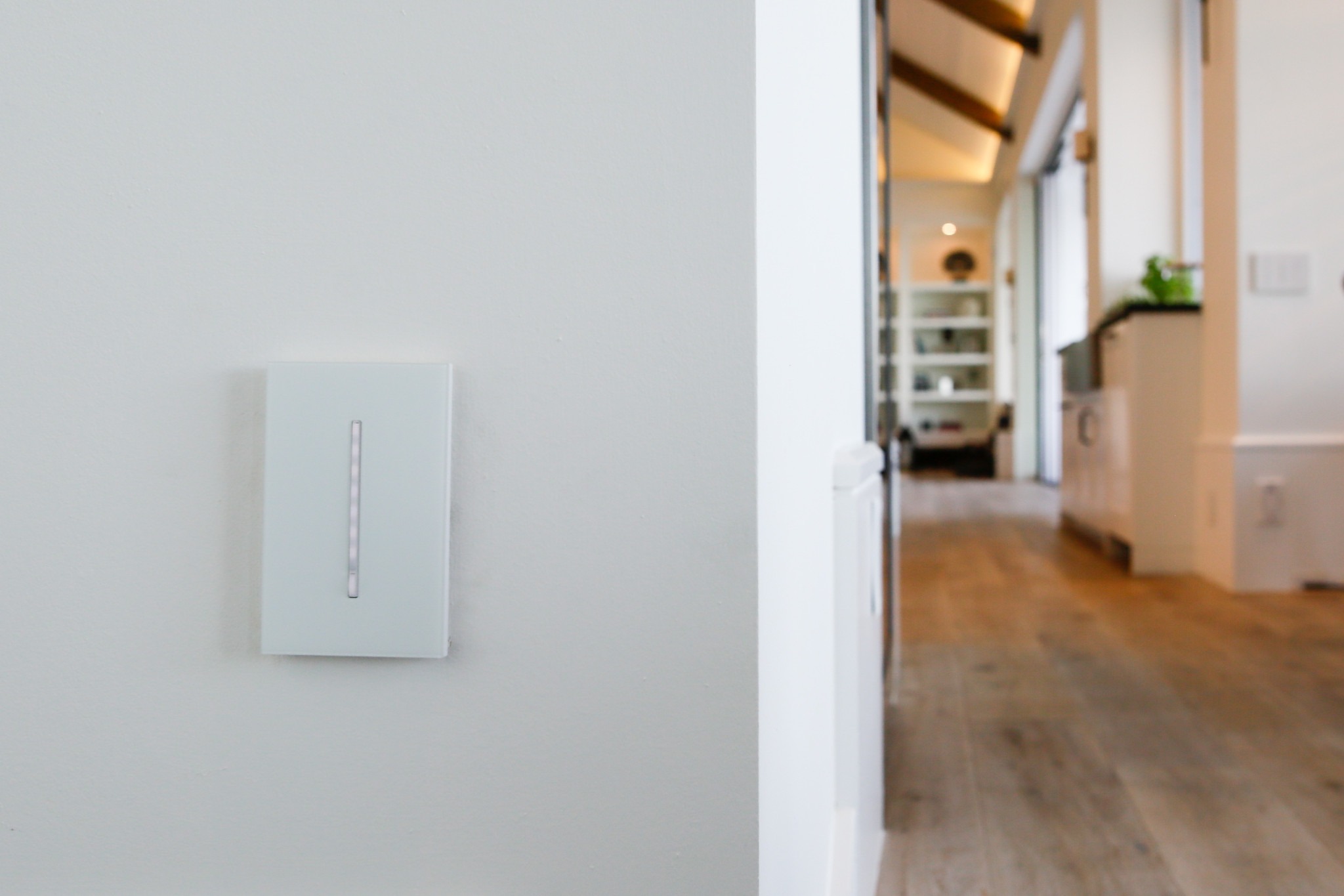 Modern interior hallway with a sleek light switch on the wall. Wooden flooring, white walls, and open shelving create a minimalist, airy ambiance.