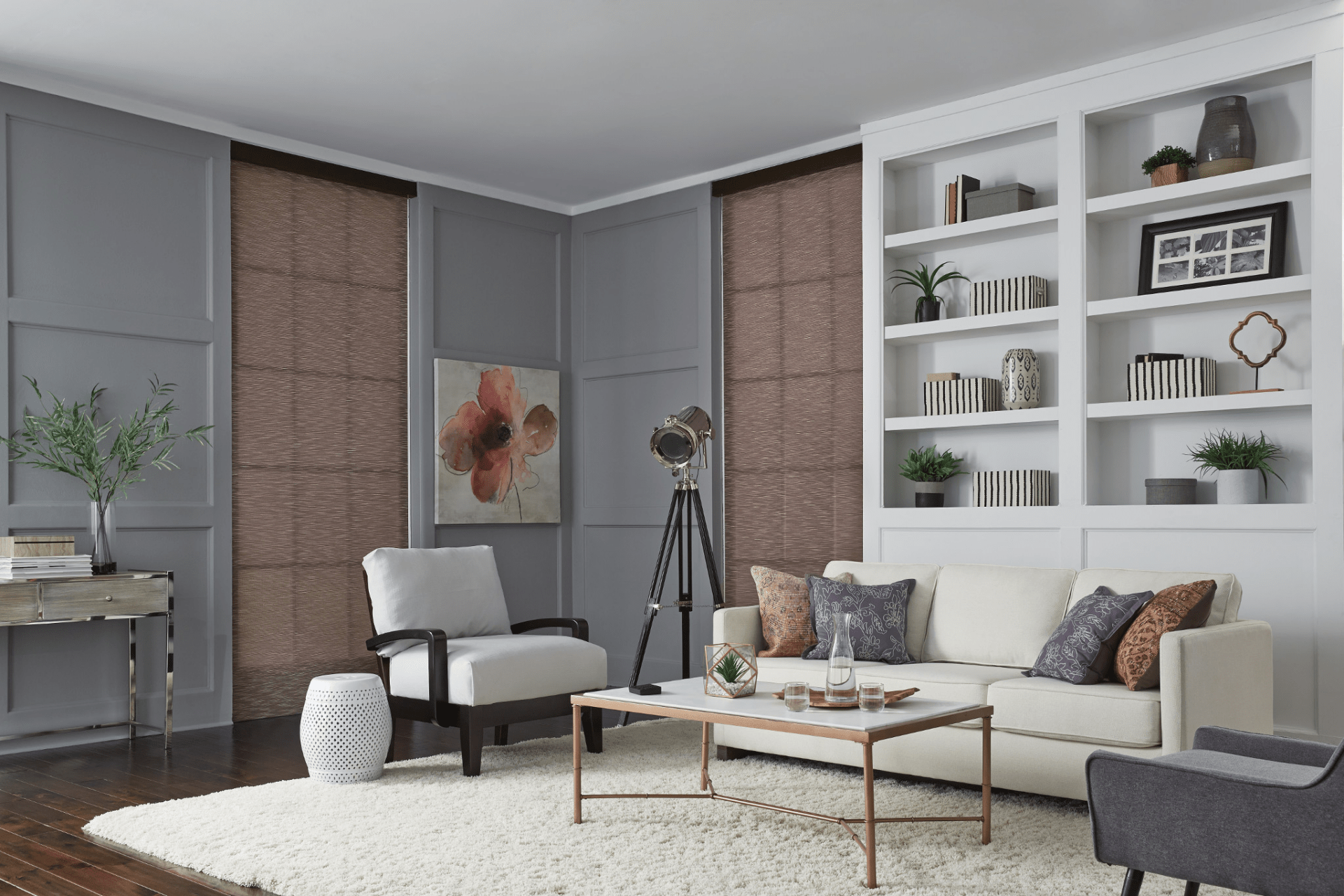 A modern living room with gray paneling, a white sofa, bookshelves, plants, artwork, and a floor lamp on a light rug.