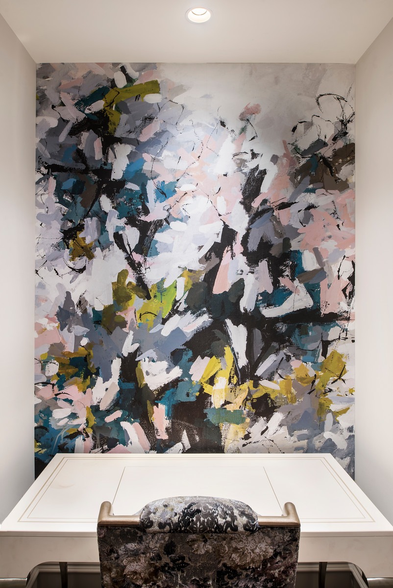 Abstract mural featuring bold, colorful brushstrokes decorates a small, modern office space with a sleek desk and an upholstered chair, creating a vibrant atmosphere.