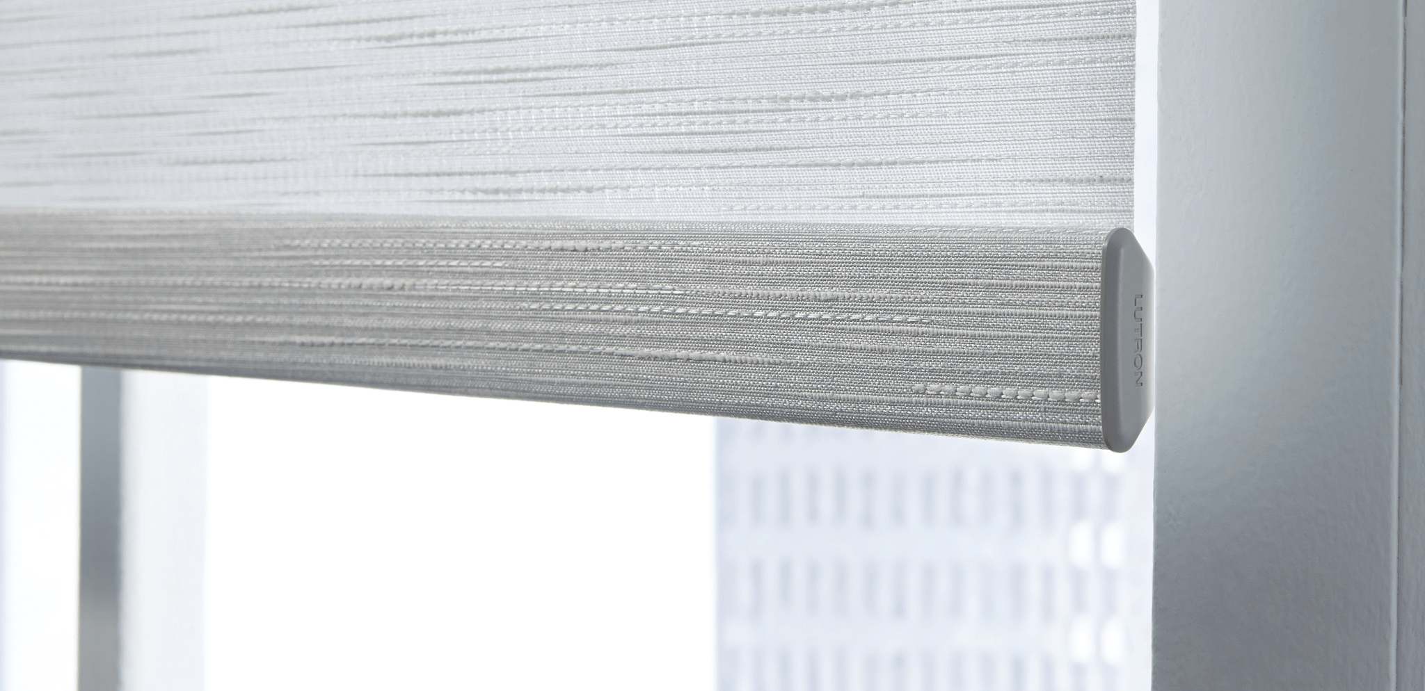 A close-up of a partially rolled-down window shade with a textured, light gray pattern. Soft natural light filters through the fabric.