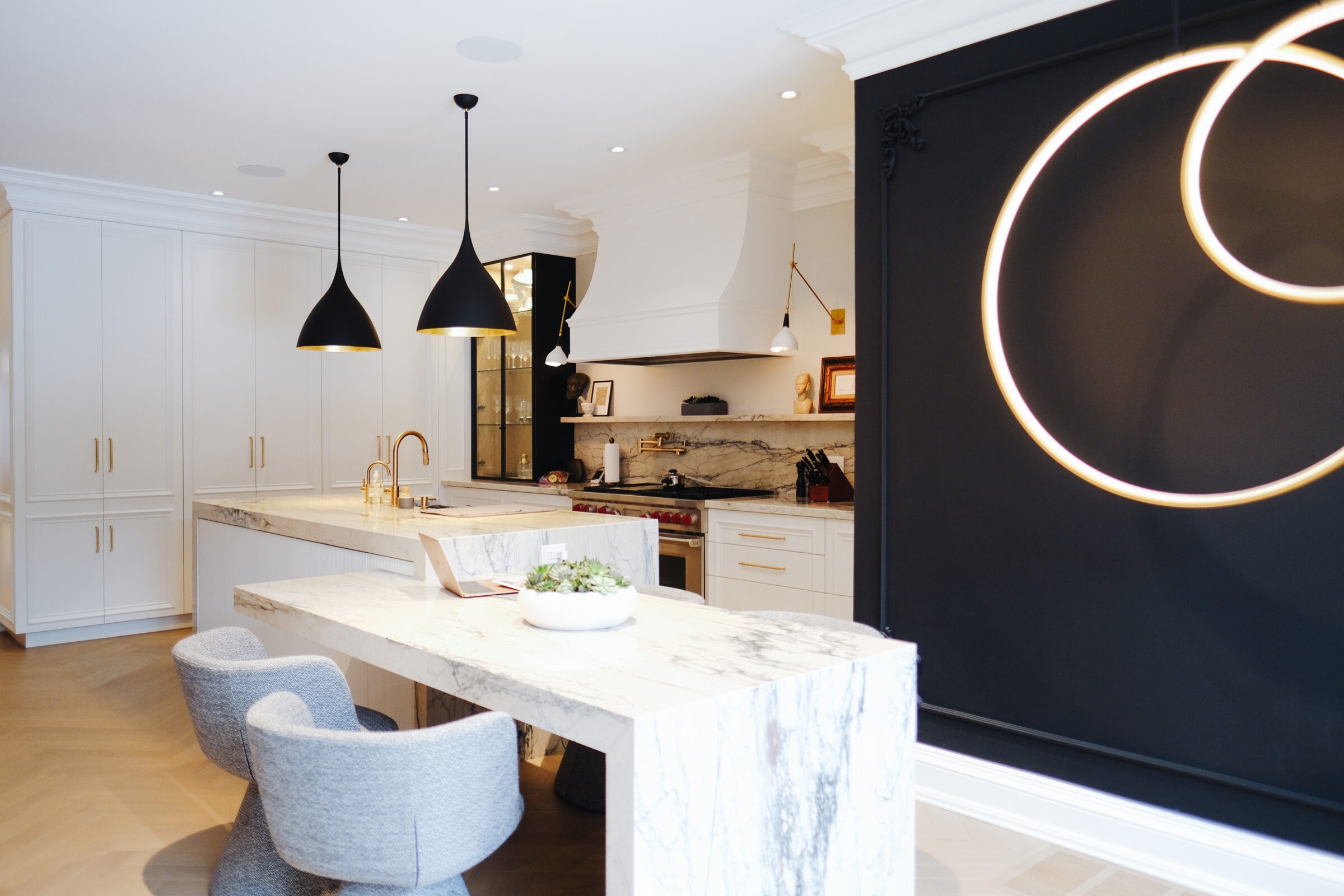 Modern kitchen with marble island, sleek cabinetry, and black accents. Two pendant lights hang above, and circular wall lights add a contemporary touch.