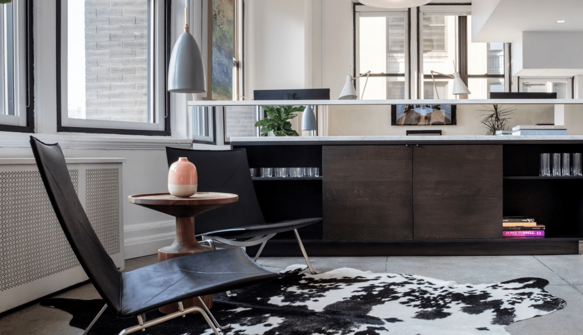 Modern interior with black chairs, cowhide rug, and a small table. Large windows and minimalist decor create an airy, contemporary atmosphere.