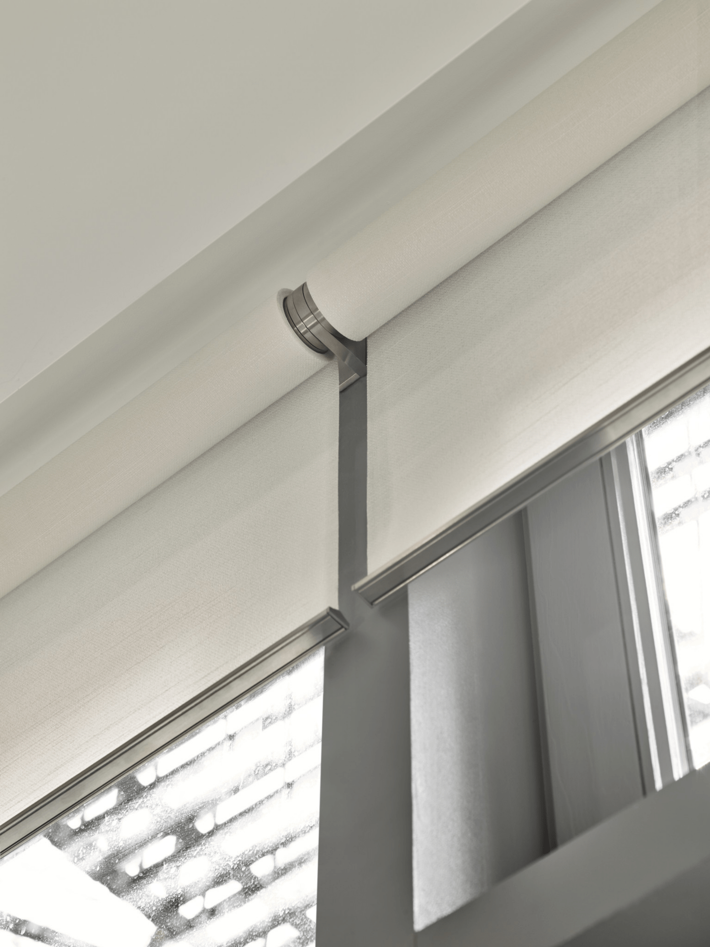 Close-up of beige roller shades on a modern window, partially open, allowing soft light to filter through the room from outside.