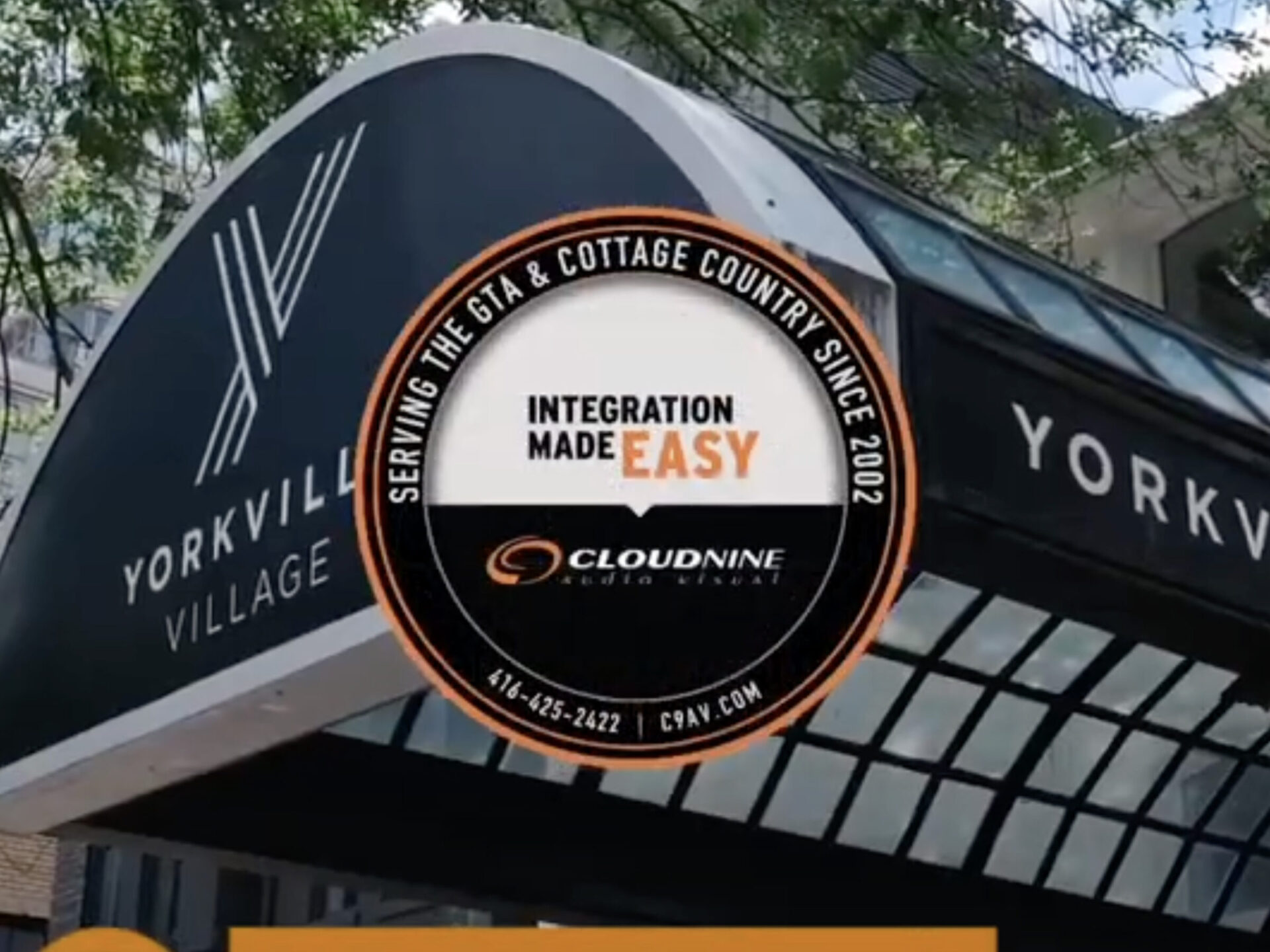 Yorkville Village entrance with a Cloudnine audiovisual services advertisement. Trees partially shade the scene. Urban setting visible in the background.