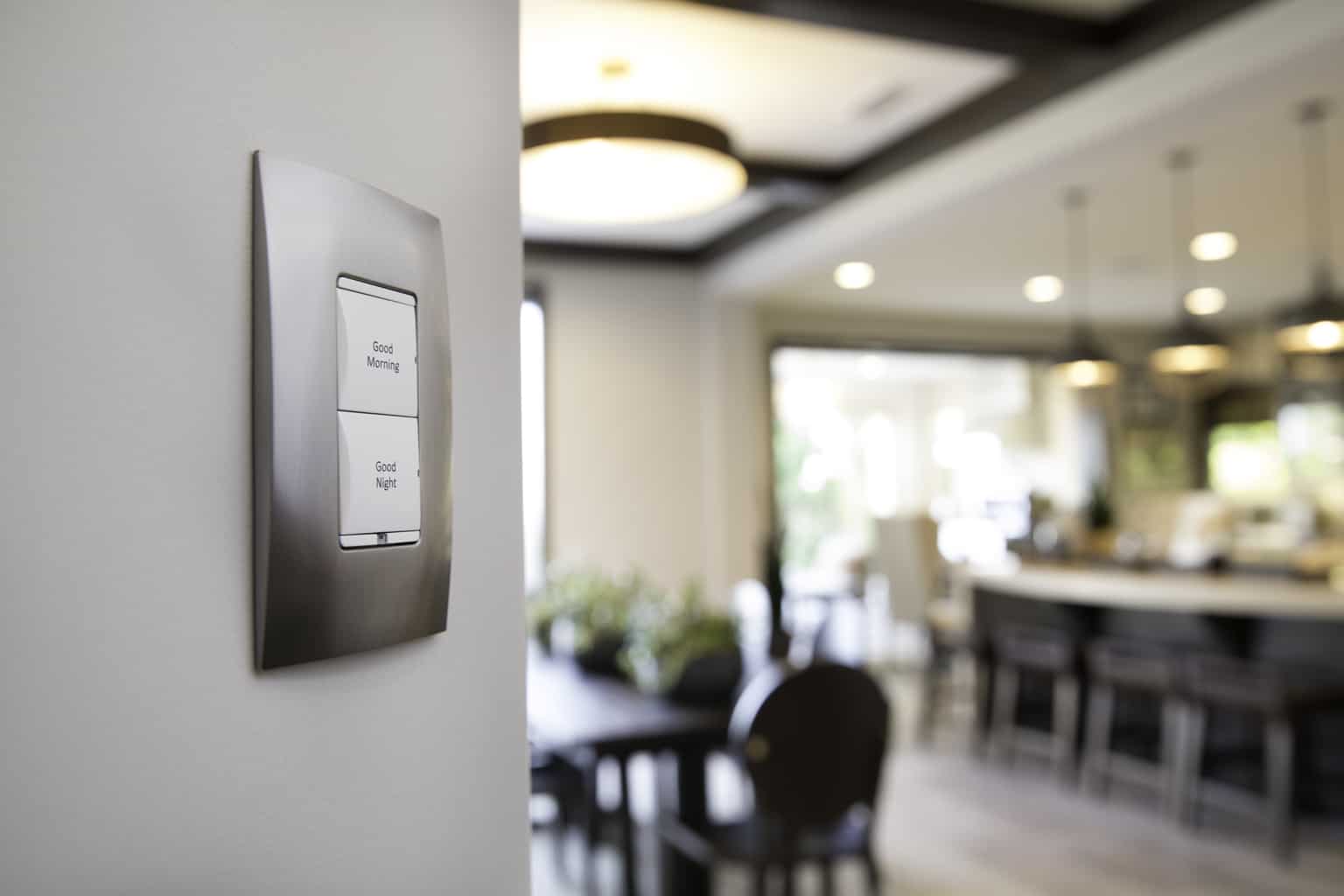 A modern interior features a sleek light switch labeled "Good Morning" and "Good Night," with a spacious kitchen and dining area in the background.