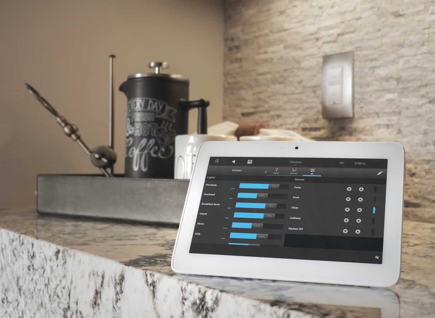 A tablet displaying a home automation app sits on a marble counter near a French press and a small tray, in a modern kitchen.