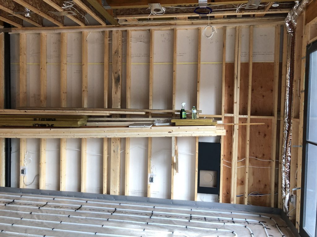 The image shows a construction site with exposed wooden framing, wiring, and insulation visible. Two shelves hold tools and materials. No people are present.