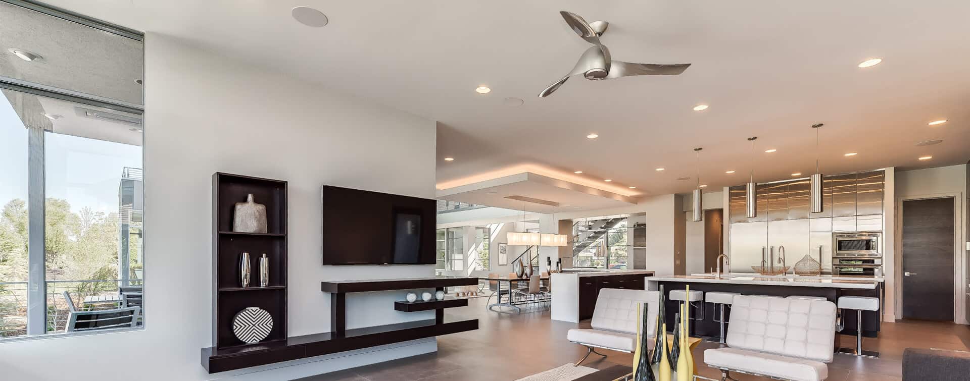 Modern open-concept living space with sleek furniture, minimalist decor, large windows, and a contemporary kitchen. Ceiling fan and flat-screen TV included.