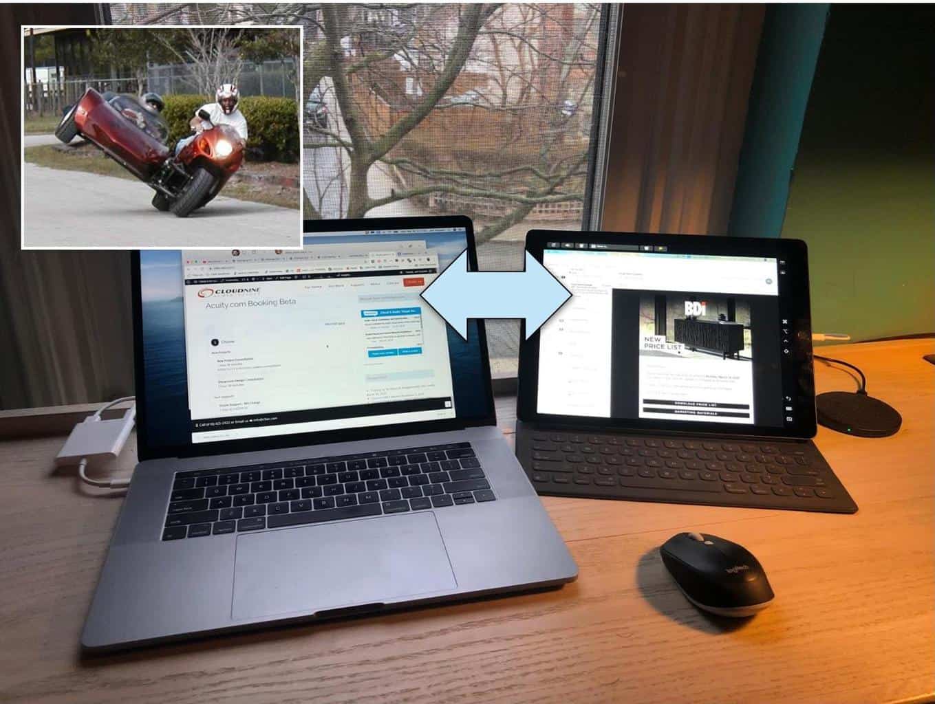 A workspace with a laptop, tablet, and mouse on a desk, featuring a humorous motorcycle photo on the wall.