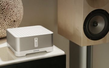 A Sonos Connect Amp is placed on a shelf next to a large speaker, with decorative accents in the background.