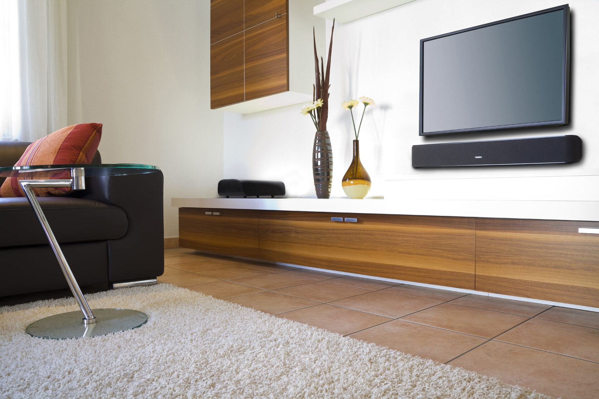 Modern living room with a sleek sofa, flat-screen TV, soundbar, glass-top table, and decorative vases on a wooden console over a plush rug.