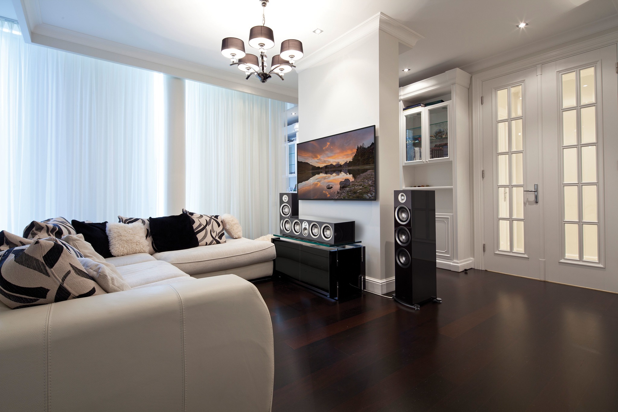 A modern living room features a large sectional sofa, a wall-mounted TV, speakers, and elegant decor with soft lighting and minimalistic design.