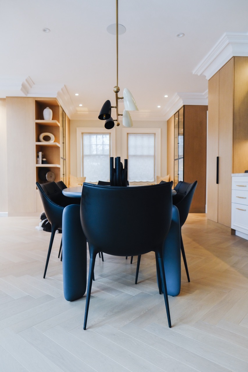 Modern dining area with sleek black chairs and a stylish ceiling lamp. Wooden flooring and built-in shelves create a cozy ambiance.