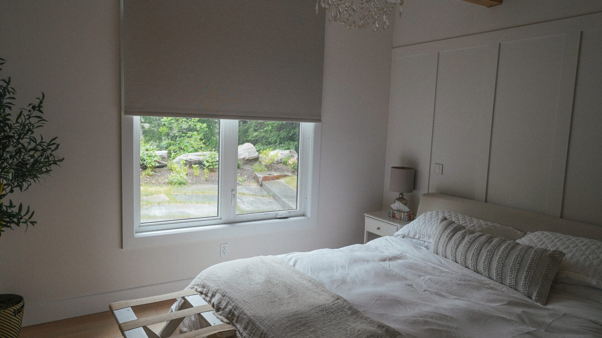 A cozy bedroom with a large bed, bedside table, and window overlooking a garden. Soft lighting and neutral tones create a calming atmosphere.