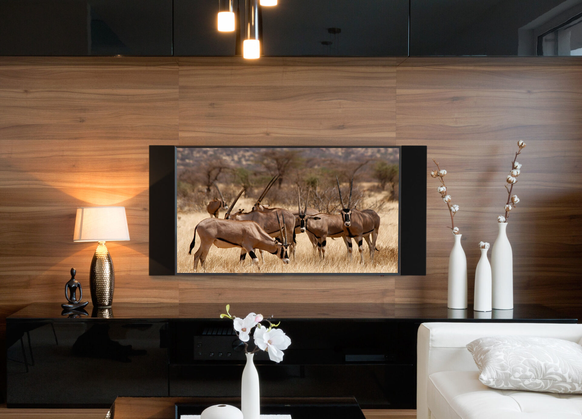 A modern living room with wooden paneling, decorative vases, and a wall-mounted TV displaying antelopes in a savanna landscape.