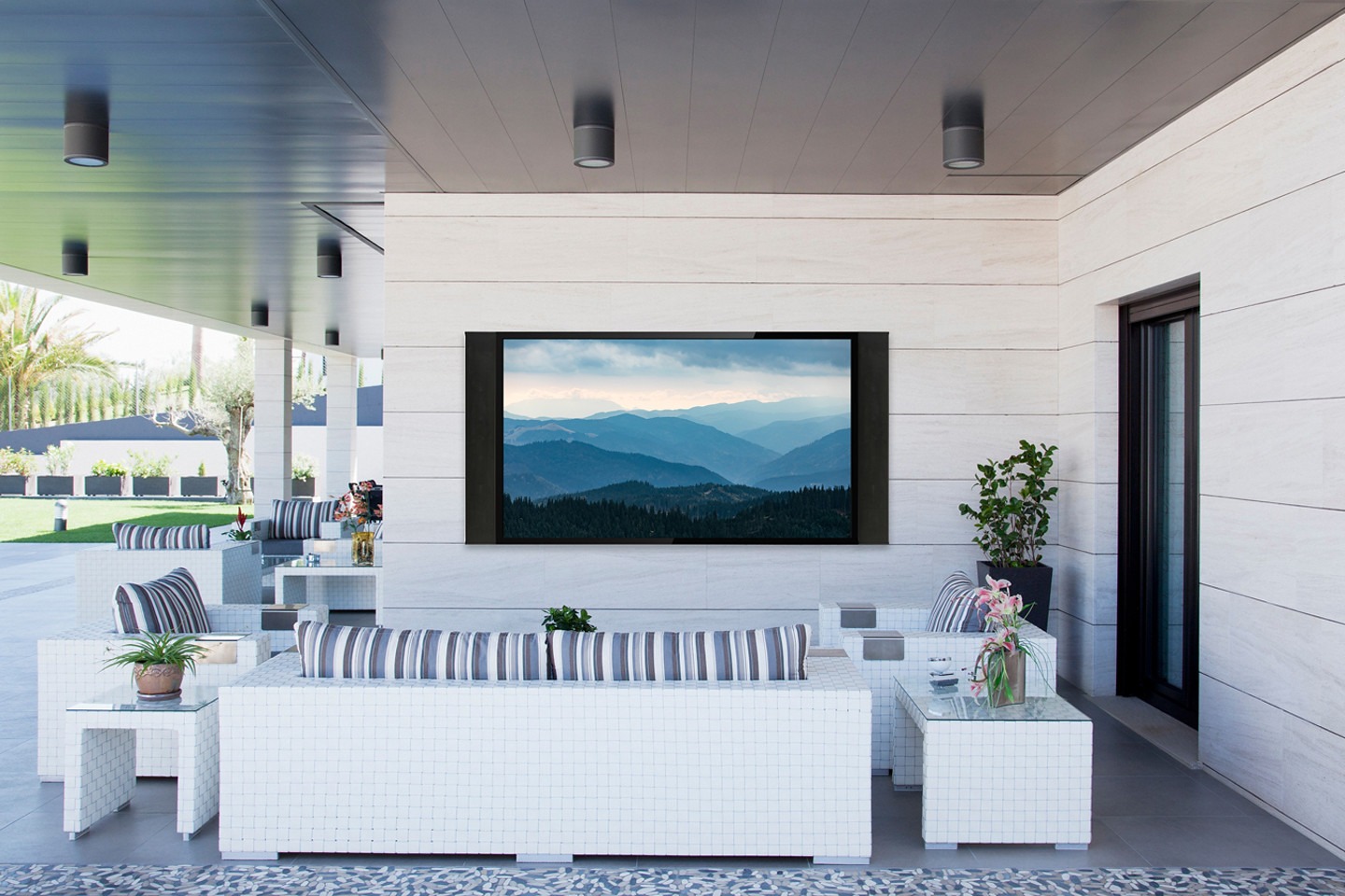 Modern patio with white furniture, striped cushions, plants, and a large screen displaying mountains. No people or landmarks visible. Bright and spacious design.