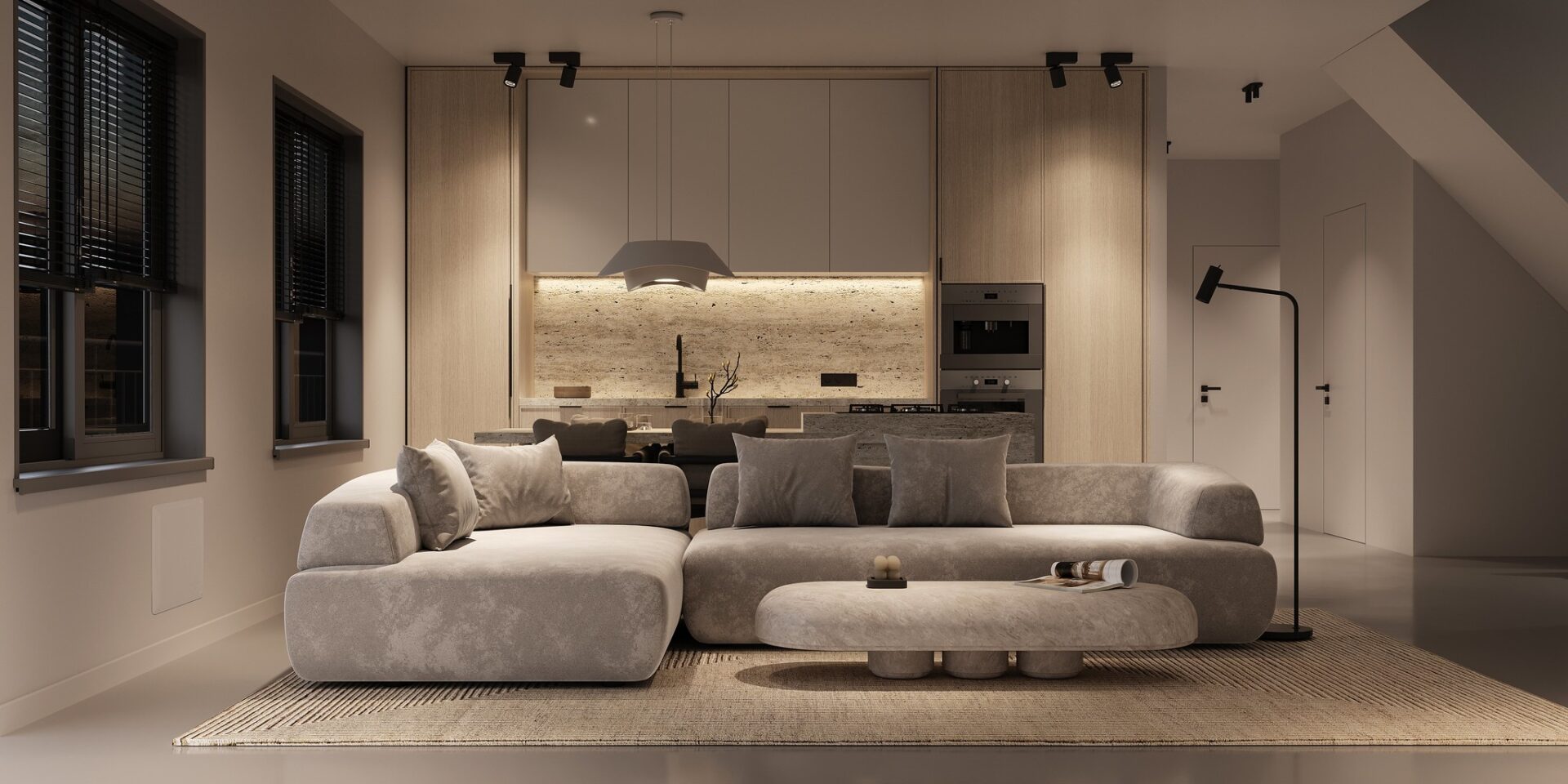 Modern living room with minimalist design, featuring a large gray sofa, low coffee table, open-plan kitchen, warm lighting, and neutral color palette.