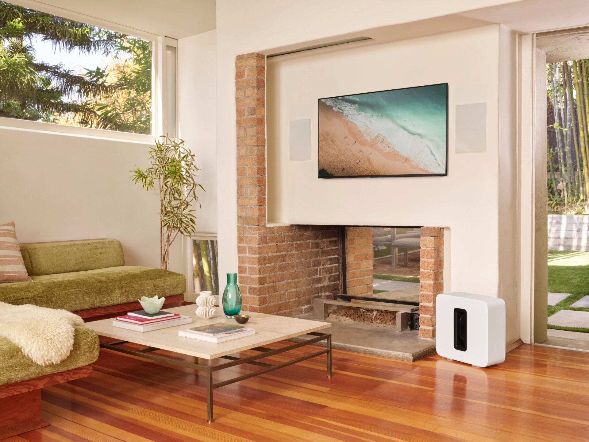 Modern living room with a brick fireplace and stylish decor. Large window, greenery outside, and a sleek wall-mounted TV above the mantel.