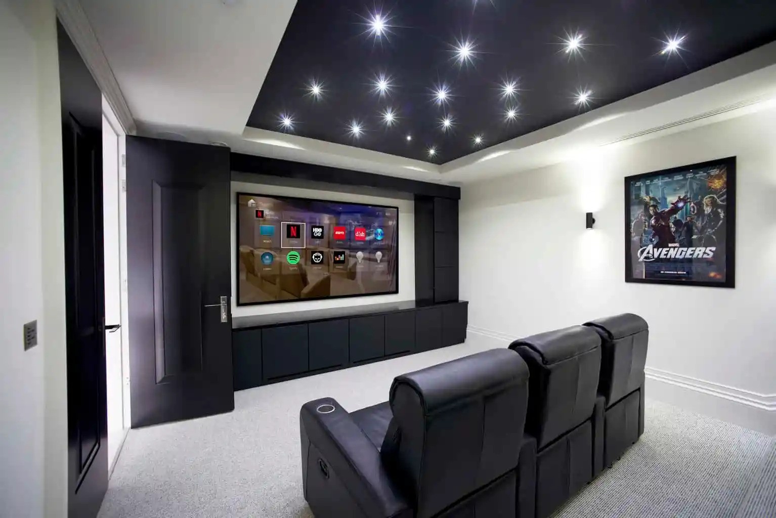 Home theater room with three reclining seats, a large screen, starry ceiling lights, and an Avengers poster on the wall.