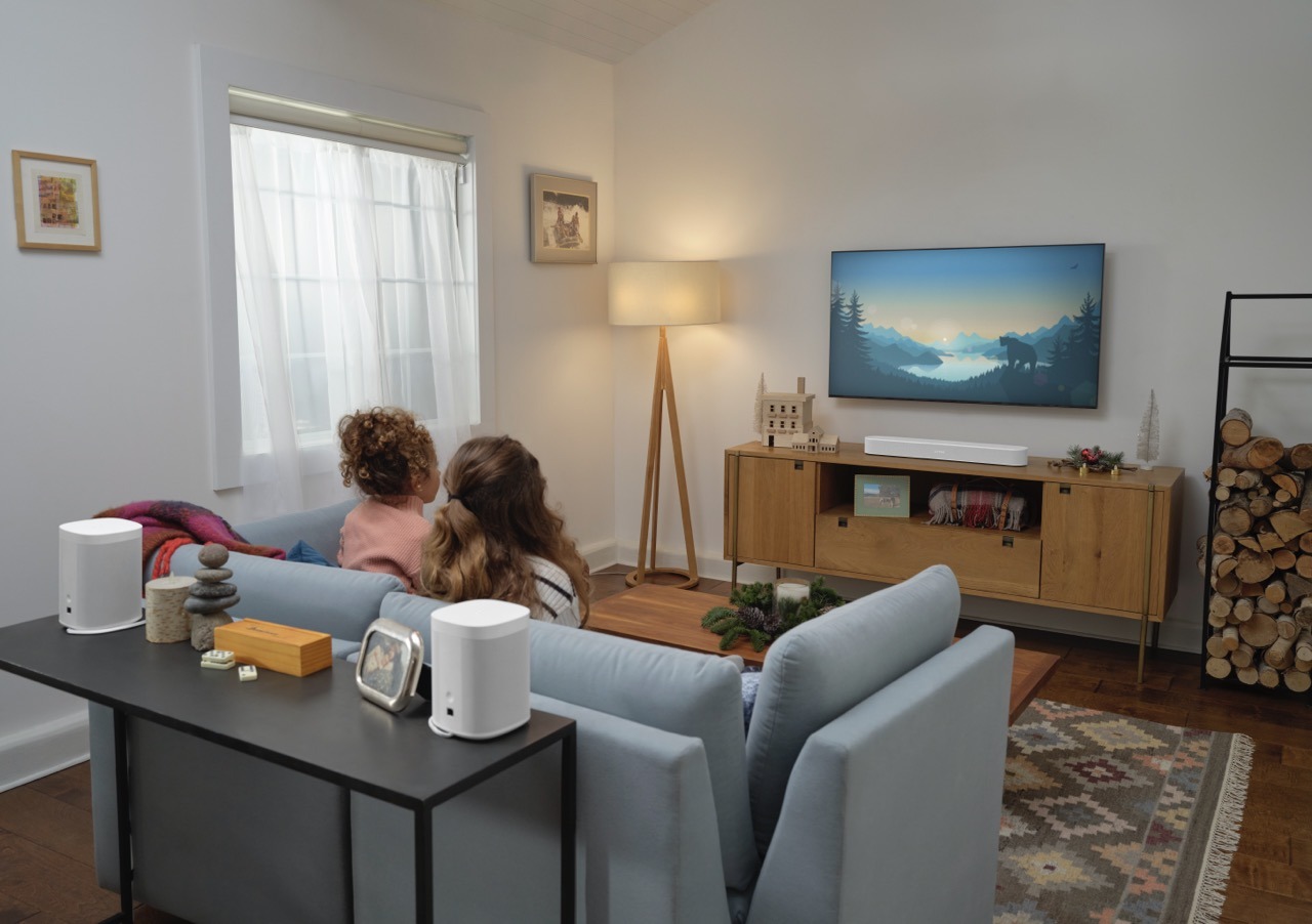 A cozy living room with two people watching TV. The room is decorated with modern furniture, art, and stacked firewood beside a console table.