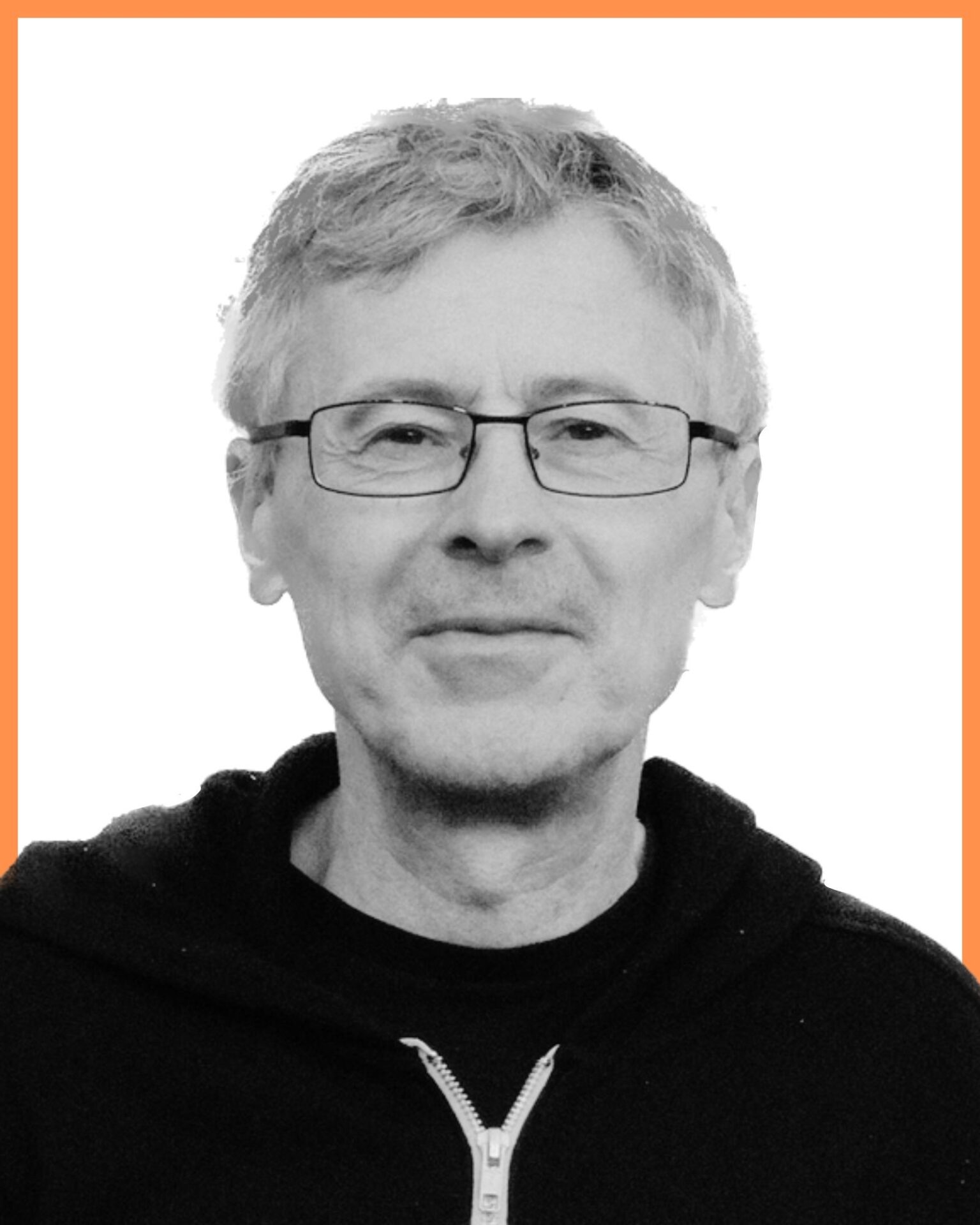 A person with short hair and glasses wearing a dark zip-up hoodie stands against a plain white background with an orange border.