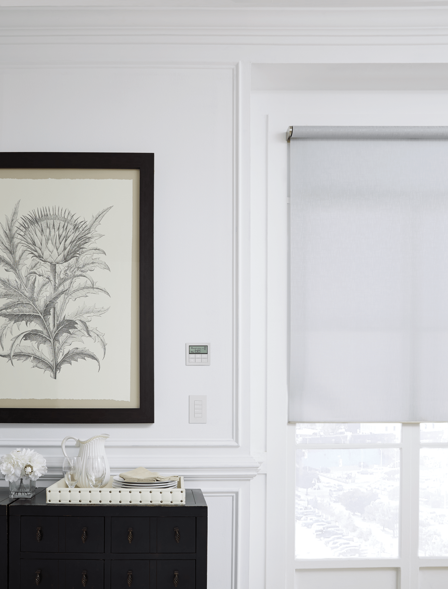 A bright, elegant room features a botanical print, a black cabinet with decor, and a window with a pale blind, streaming soft light.