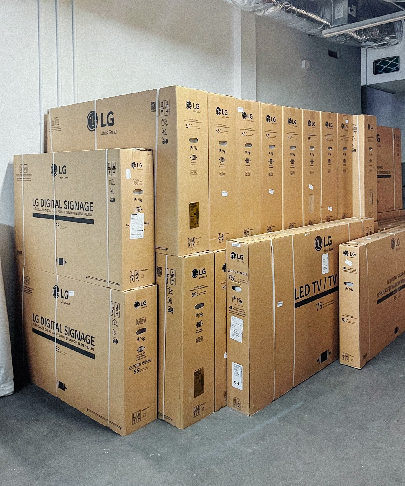 A stack of LG TV and digital signage boxes is arranged along a wall in a storage or warehouse area.