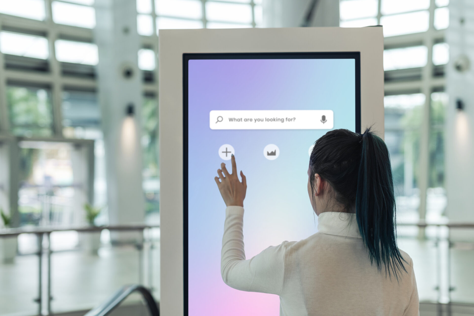 A person interacts with a large touchscreen in a modern interior, which has tall glass windows and a circular ceiling design.