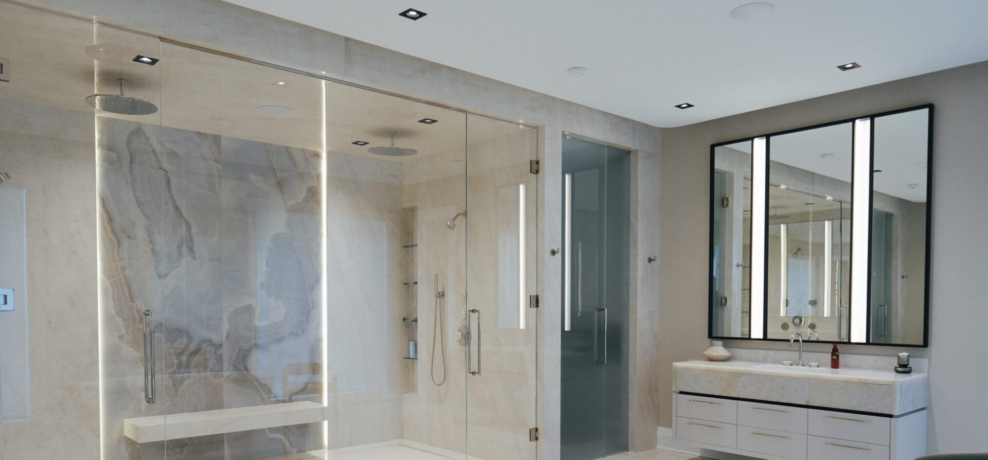 Spacious, modern bathroom with glass shower, large mirror, and sleek marble finishes. Bright lighting and minimalistic design create a luxurious atmosphere.