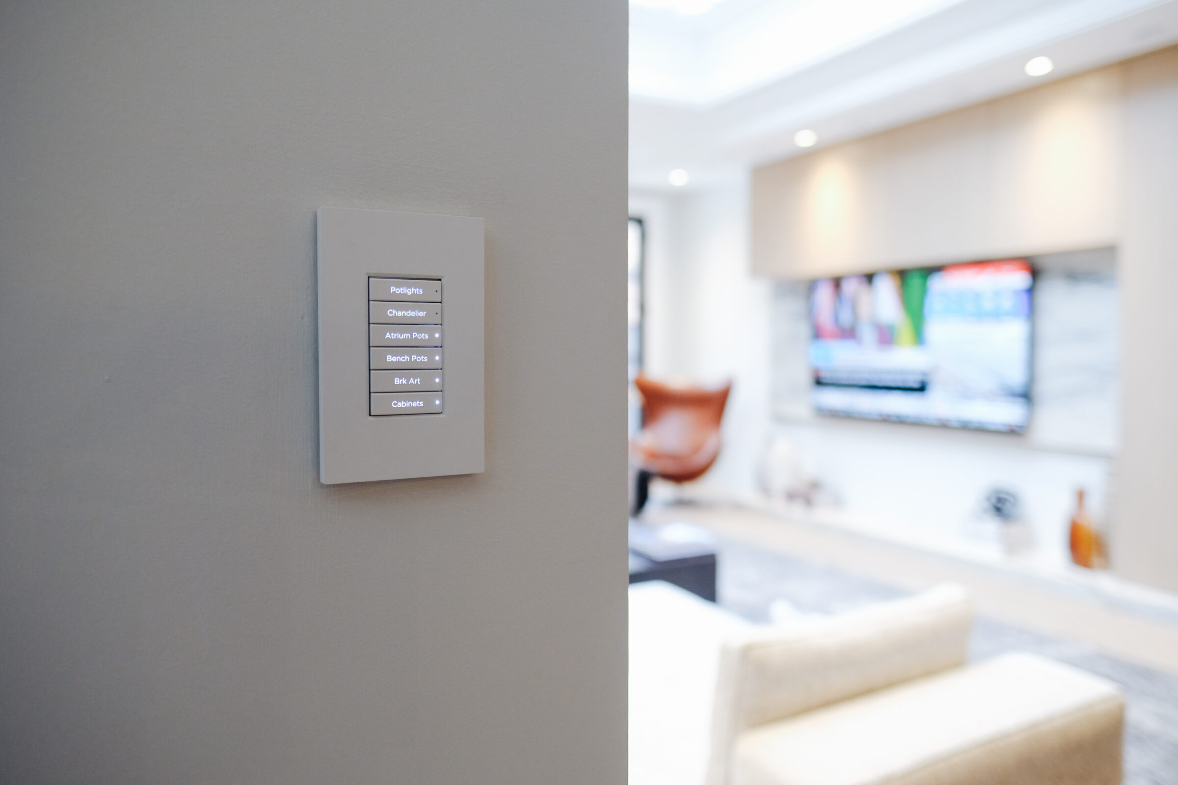 Modern living room with a wall-mounted smart home control panel and a large TV. The room appears bright and comfortable with contemporary furniture.