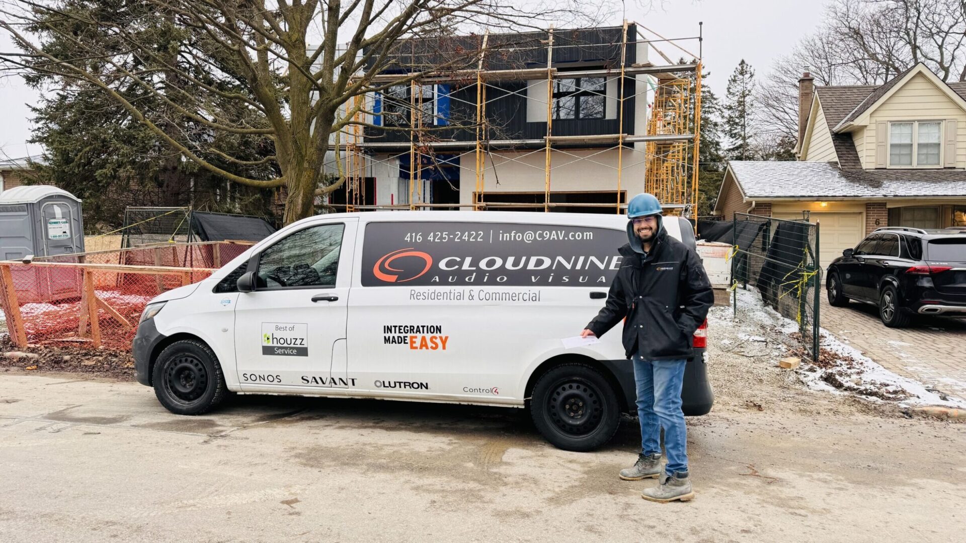 A person in a helmet stands beside a van labeled "Cloud9 AV" in front of a partially constructed house with scaffolding.