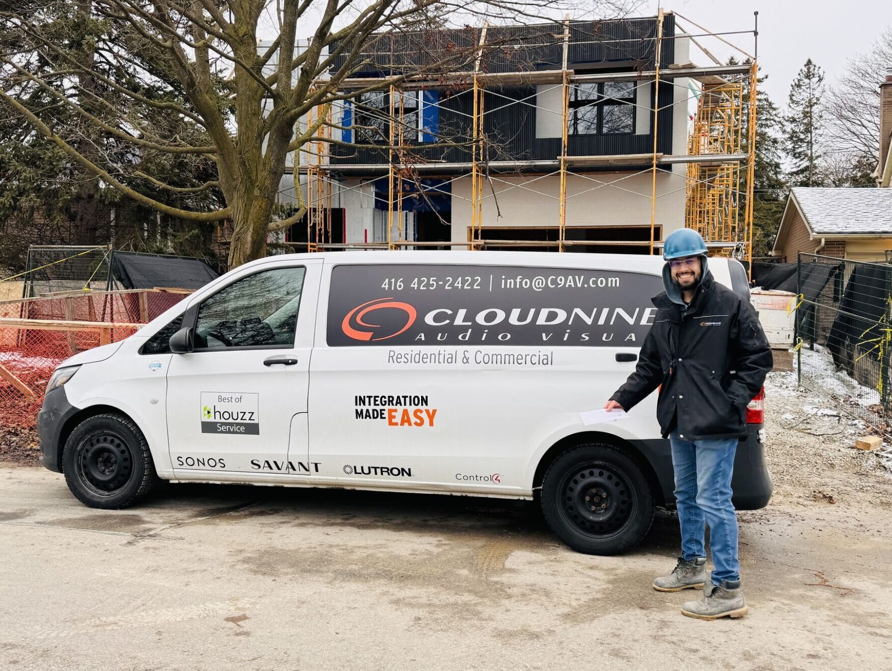 A person in a helmet stands beside a van labeled "Cloud9 AV" in front of a partially constructed house with scaffolding.