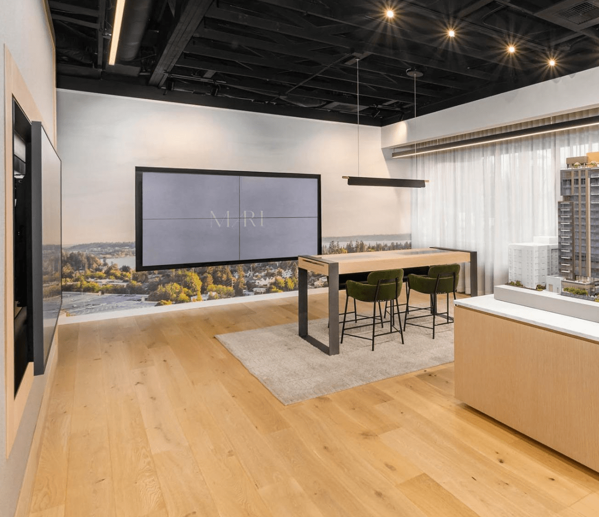 Modern showroom with a large screen, wooden floors, and a sleek table with chairs. A city skyline image is displayed on the wall.