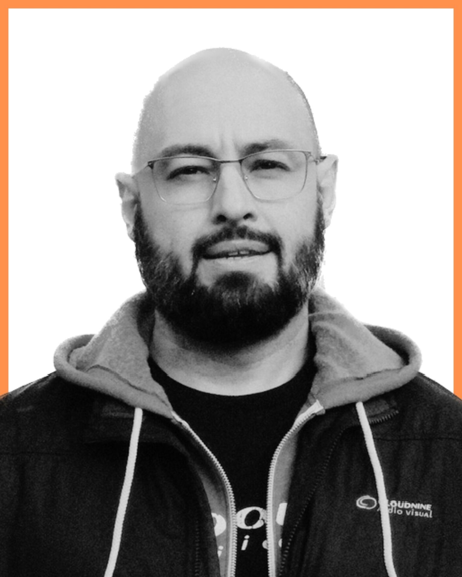 A person with glasses and a beard is wearing a hooded jacket. The image has an orange border and a plain white background.