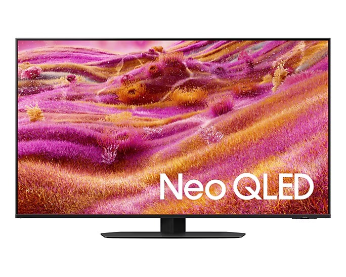 A black-framed Neo QLED television displays a vibrant, abstract pink and orange landscape. The screen stands on a central black pedestal base. Samsung 2025 TV for your home